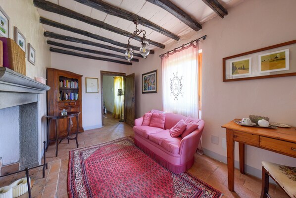 A cozy living room with a pink sofa, a fireplace, a wooden table, and a red patterned rug.