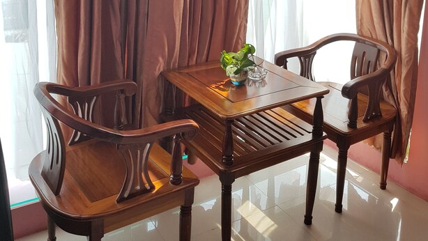 Een eethoek met een houten tafel en stoelen, een potplant en lichte gordijnen.