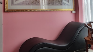 Een kamer met een groot schilderij van een straatbeeld, een zwarte bank en een houten stoel.