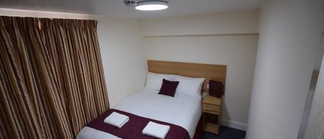 A hotel room with a single bed, a wooden headboard, a nightstand, and a window with curtains.