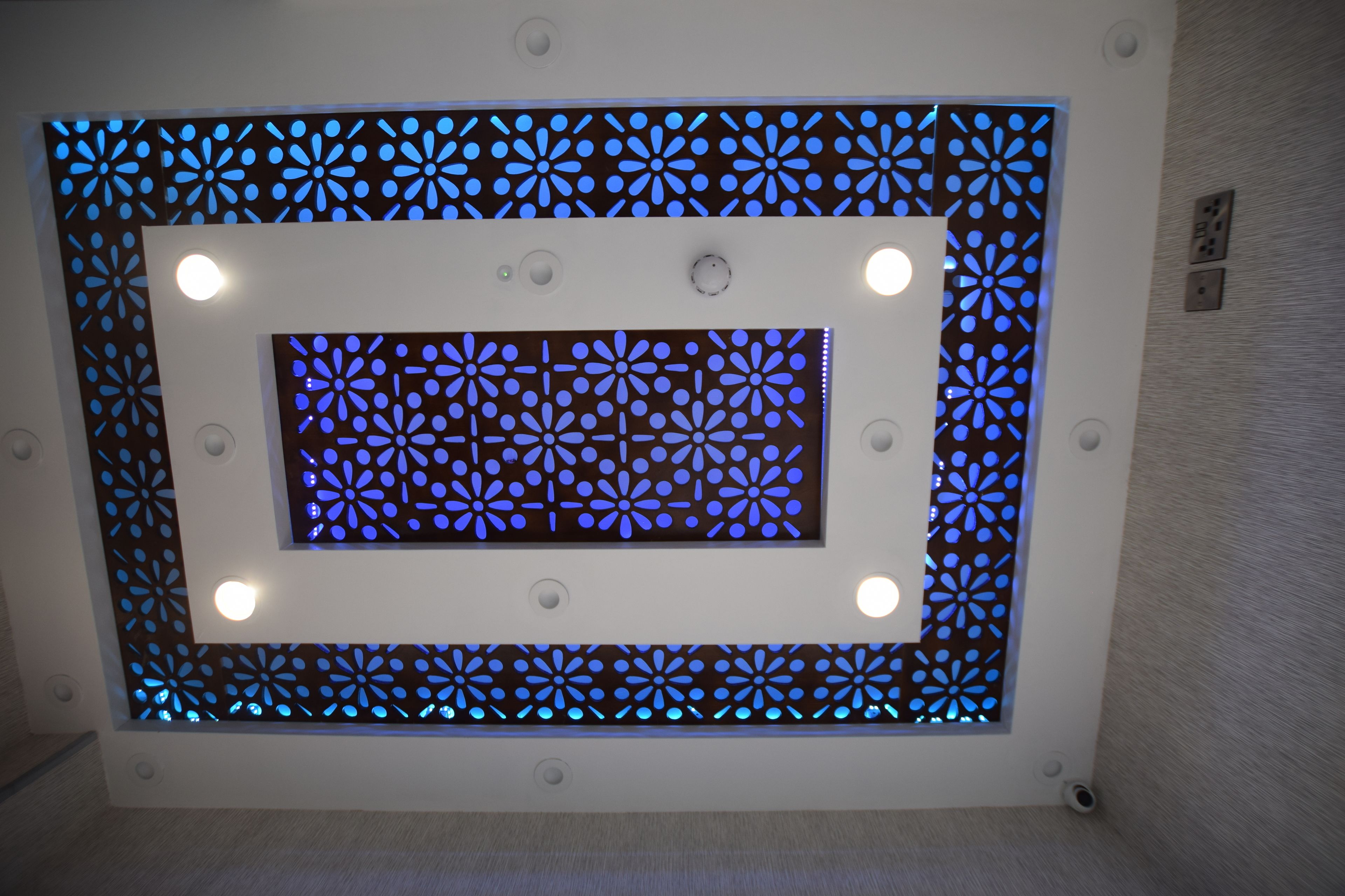 Een plafond met een decoratief paneel met een geometrisch patroon en inbouwverlichting.