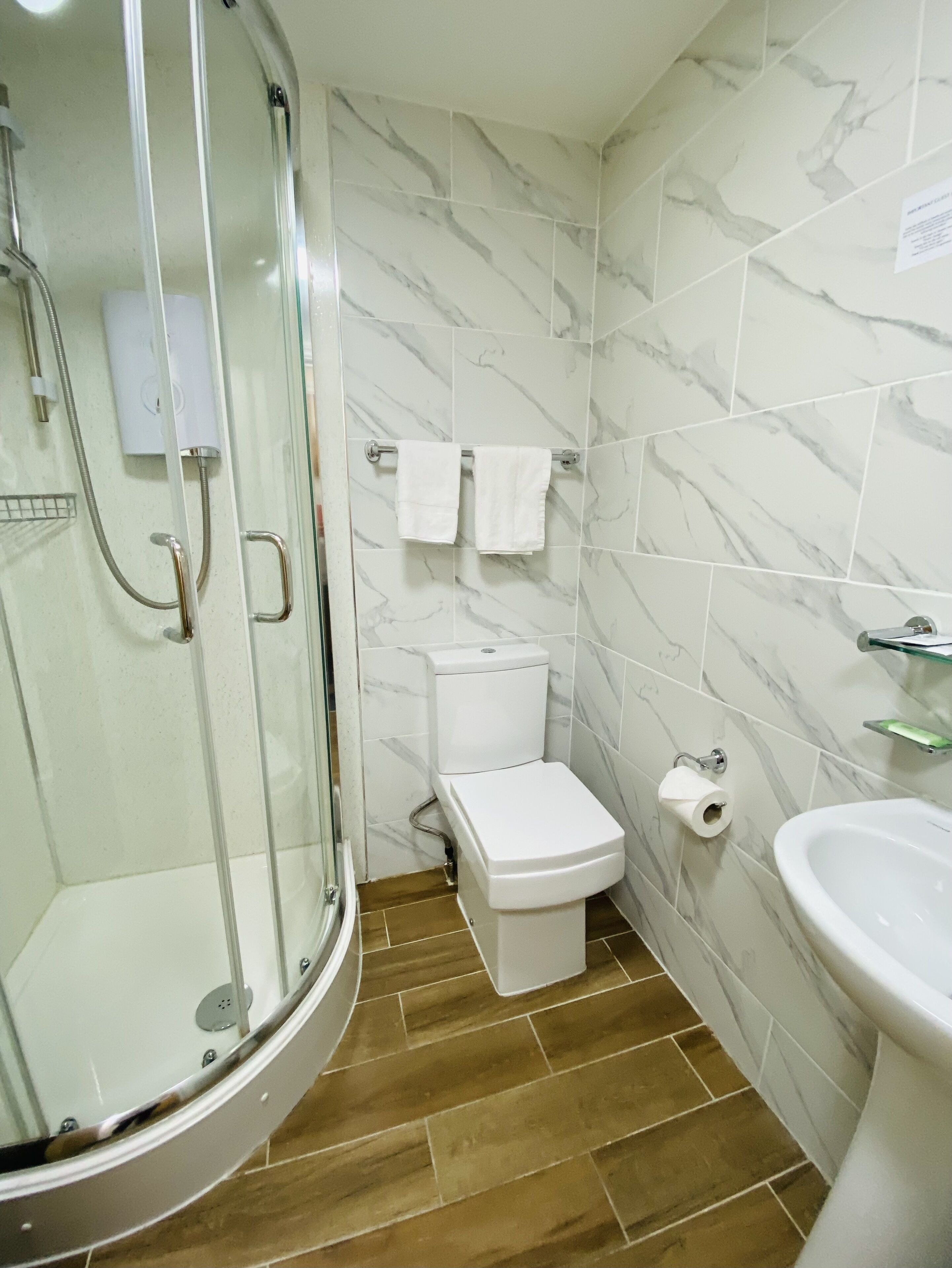 Une salle de bain dotée d’une douche à parois de verre, de toilettes, d’un lavabo et de murs aux motifs de marbre.
