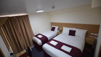 A hotel room with two beds, a wooden headboard, a nightstand, and a small table with a kettle.