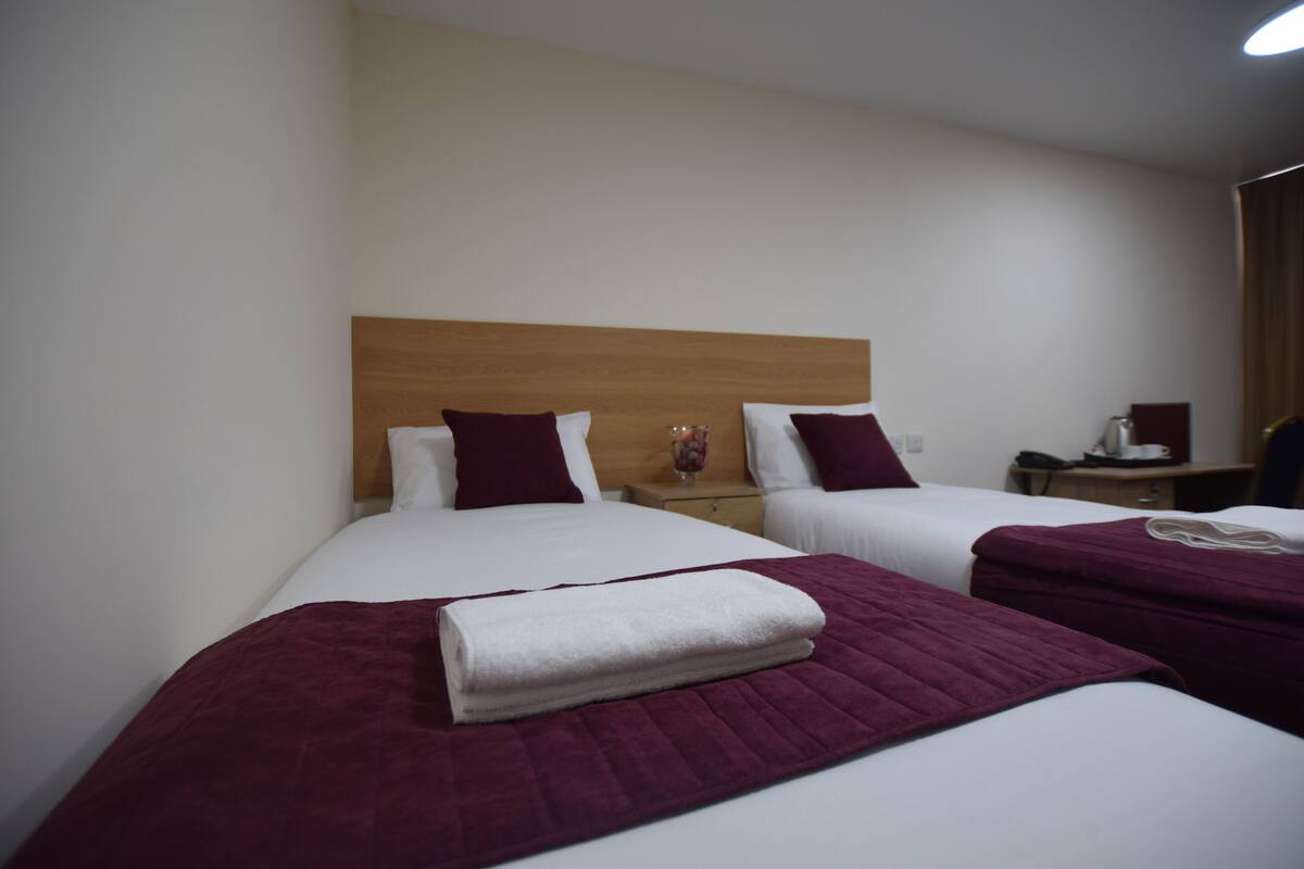 A hotel room with two beds, a wooden headboard, white linens, and a red blanket.