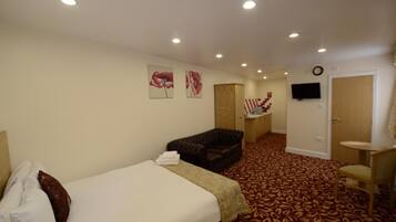 Una habitación de hotel con cama, sofá, escritorio con silla y televisor en la pared.