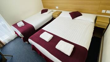 Hotellihuoneessa on kaksi erillistä sänkyä, joissa on puinen pääty, valkoiset vuodevaatteet ja tummanpunainen peitto. Huoneessa on myös puinen yöpöytä, jossa on lamppu ja pieni laatikko.