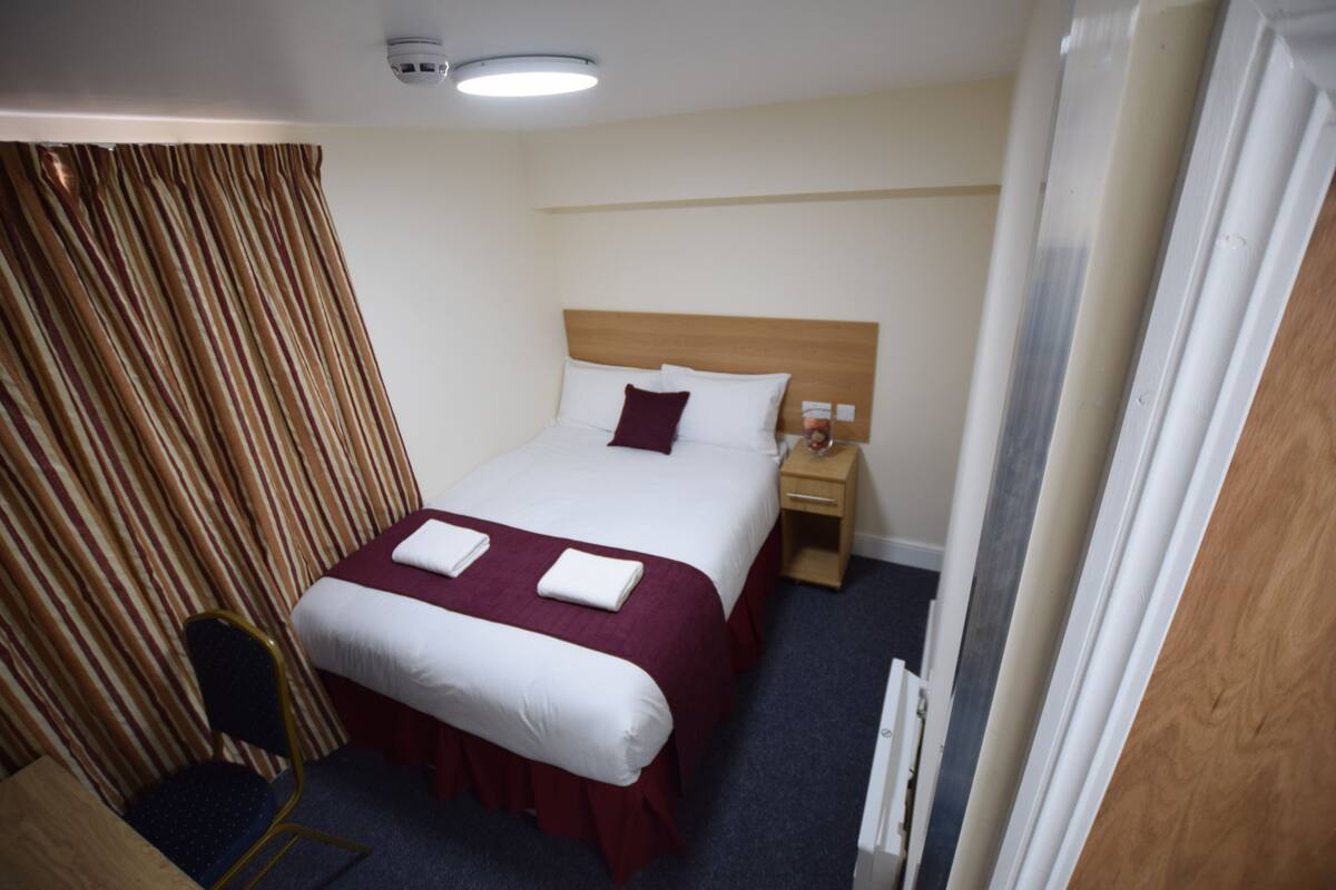A hotel room with a large bed, a bedside table, a chair, and a curtain.
