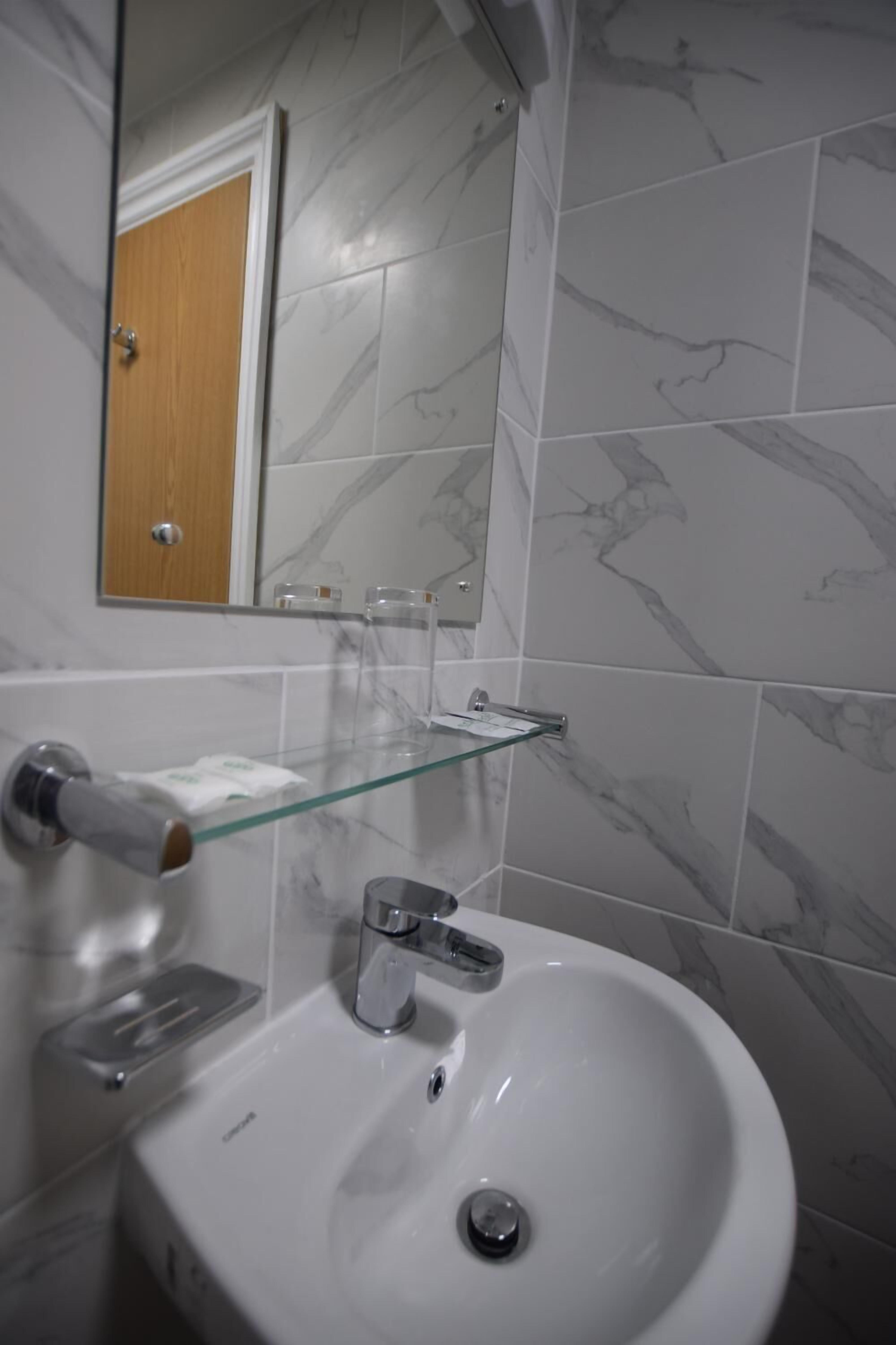 A bathroom with a white sink, a glass shelf, a mirror, and marble-patterned tiles.