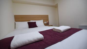 A neatly made bed with a wooden headboard, white and maroon bedding, and a white towel folded on the bed.