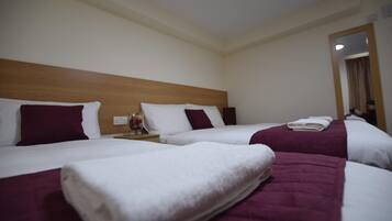A hotel room with three beds, each with white linens and maroon pillows. There is a nightstand with a glass container and a phone.