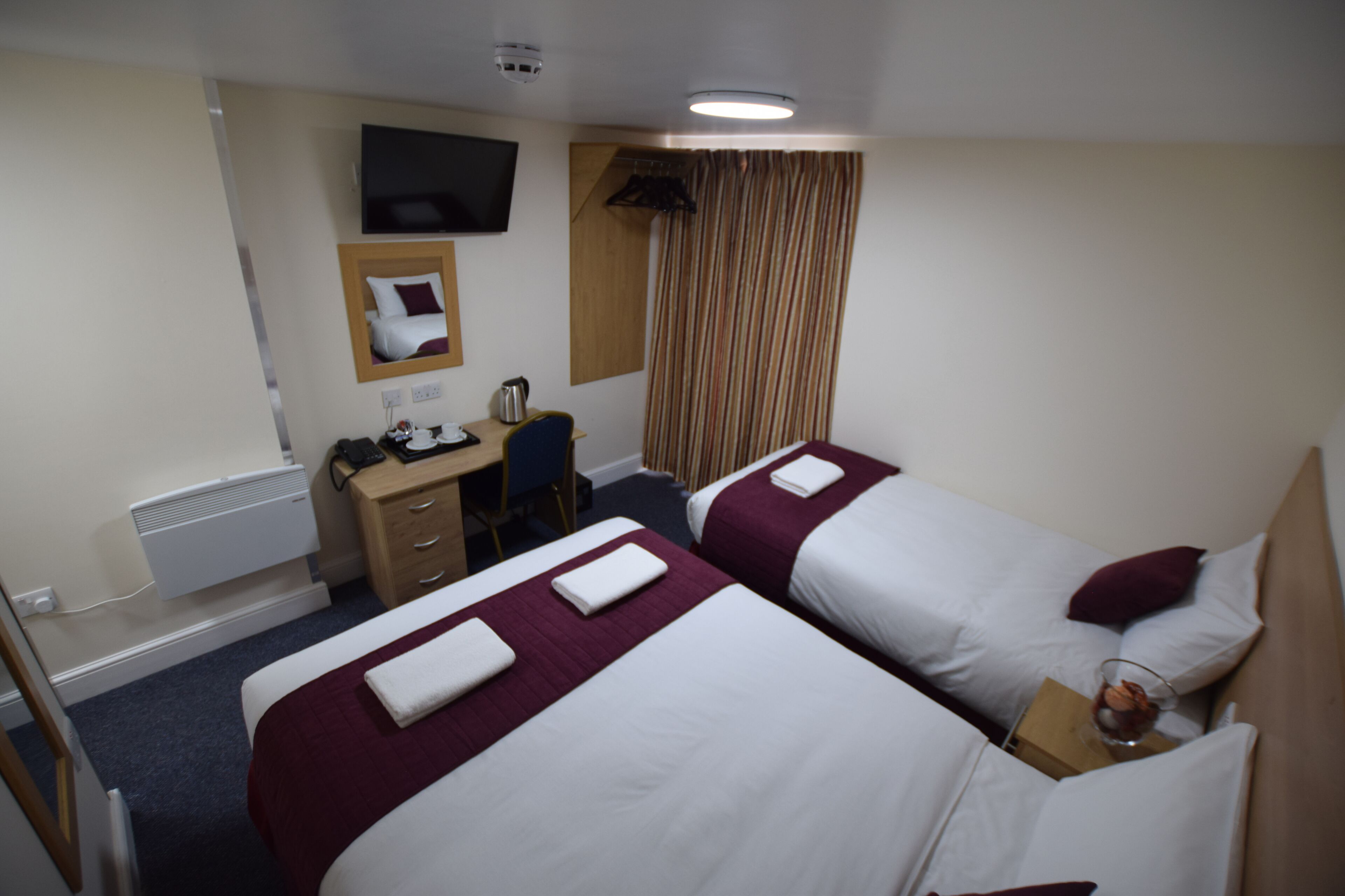 Quarto de hotel com duas camas, uma escrivaninha, uma cadeira, uma televisão e uma janela com cortinas.