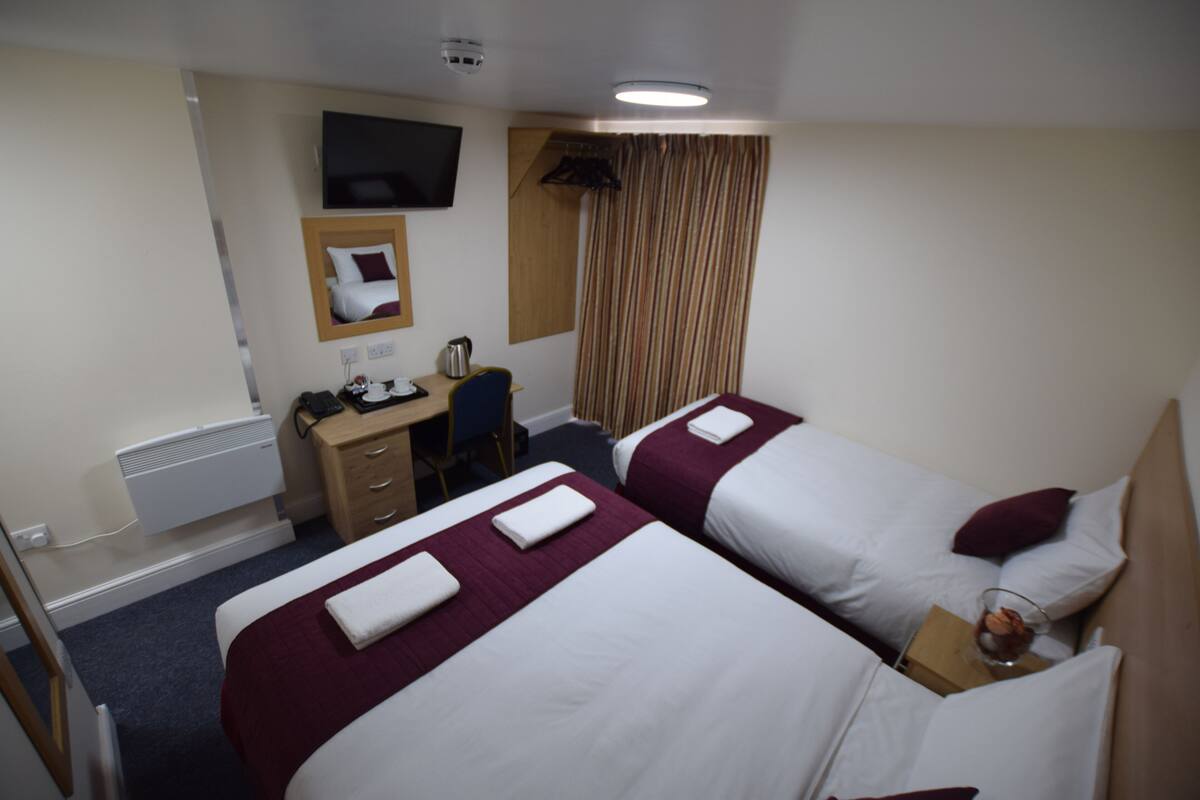 A hotel room with two beds, a desk, a chair, a television, and a window with curtains.