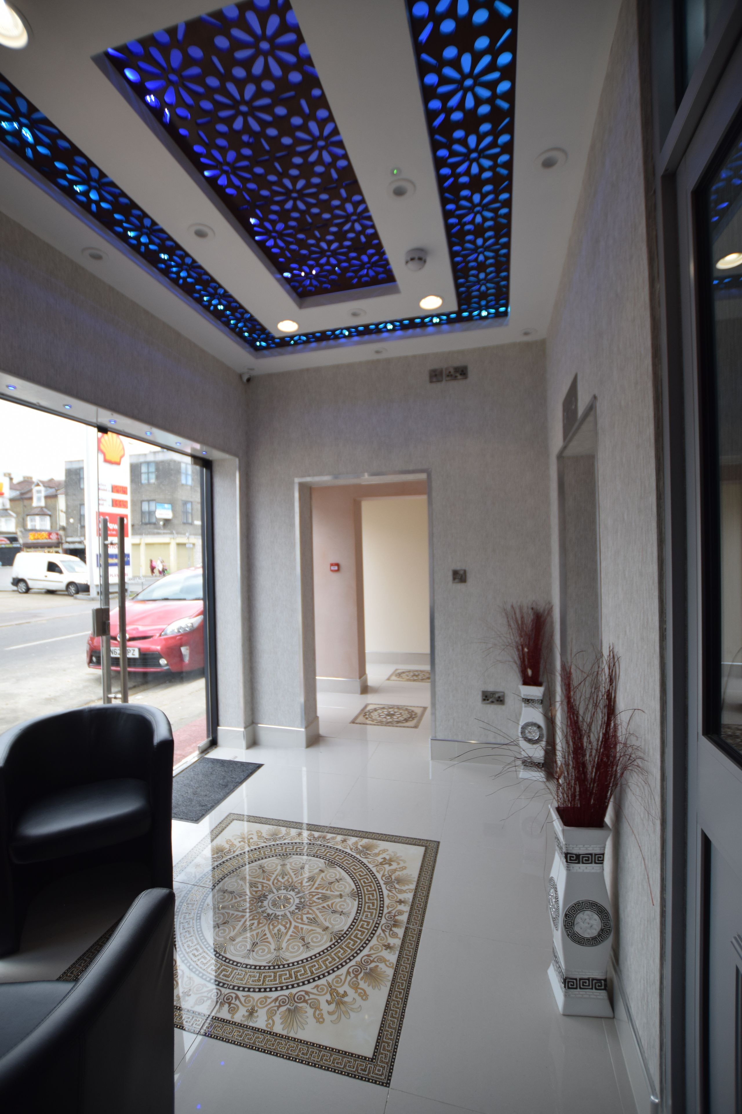 A hotel lobby with a patterned floor, a reception desk, and a decorative ceiling with blue lighting.