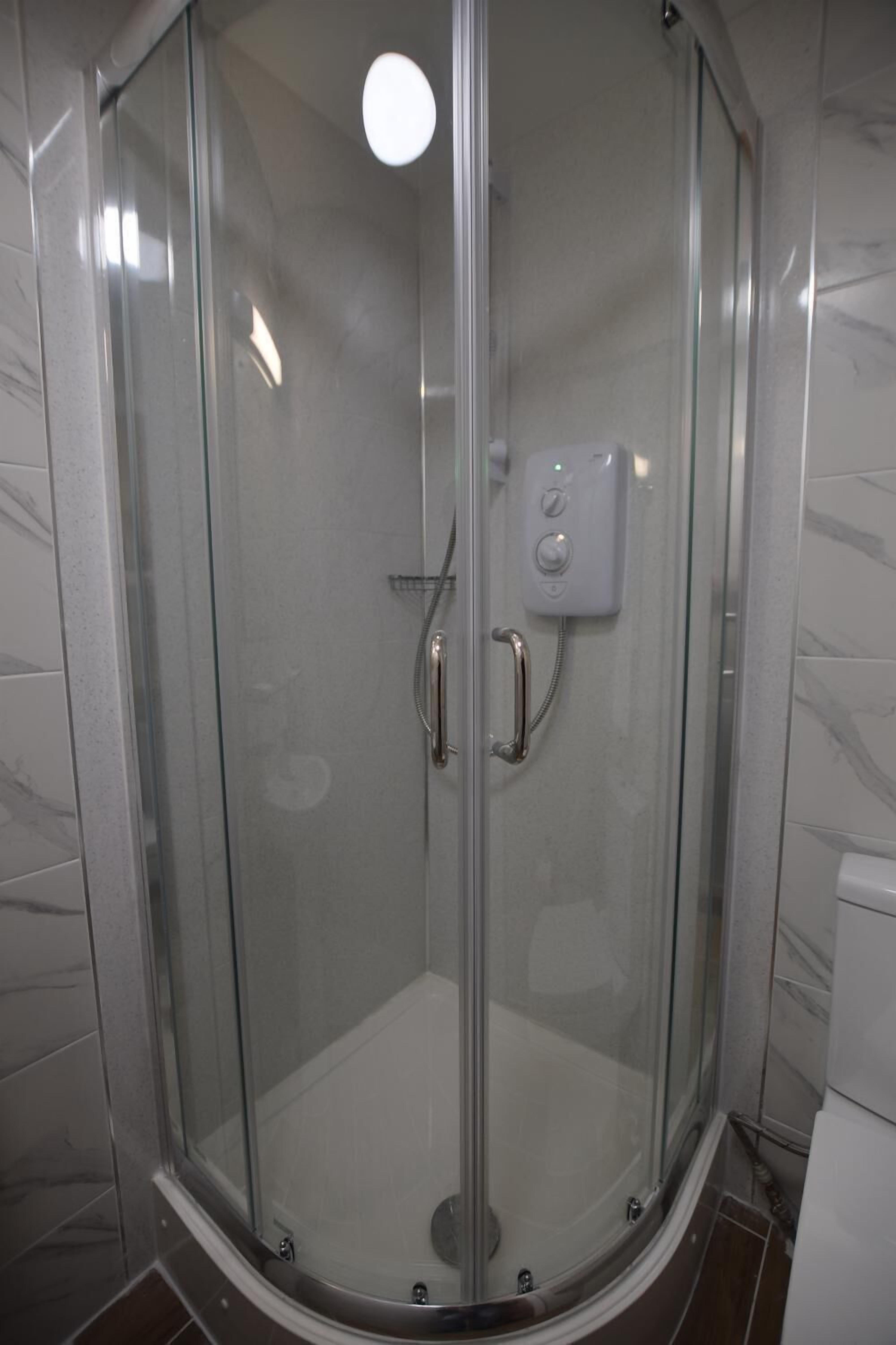 A glass-enclosed shower stall with a control panel, a handrail, and a tiled floor.