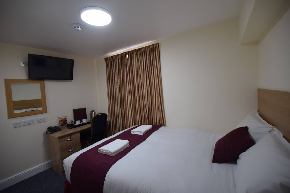 A hotel room with a bed, a desk, a chair, a television, and a window with curtains.