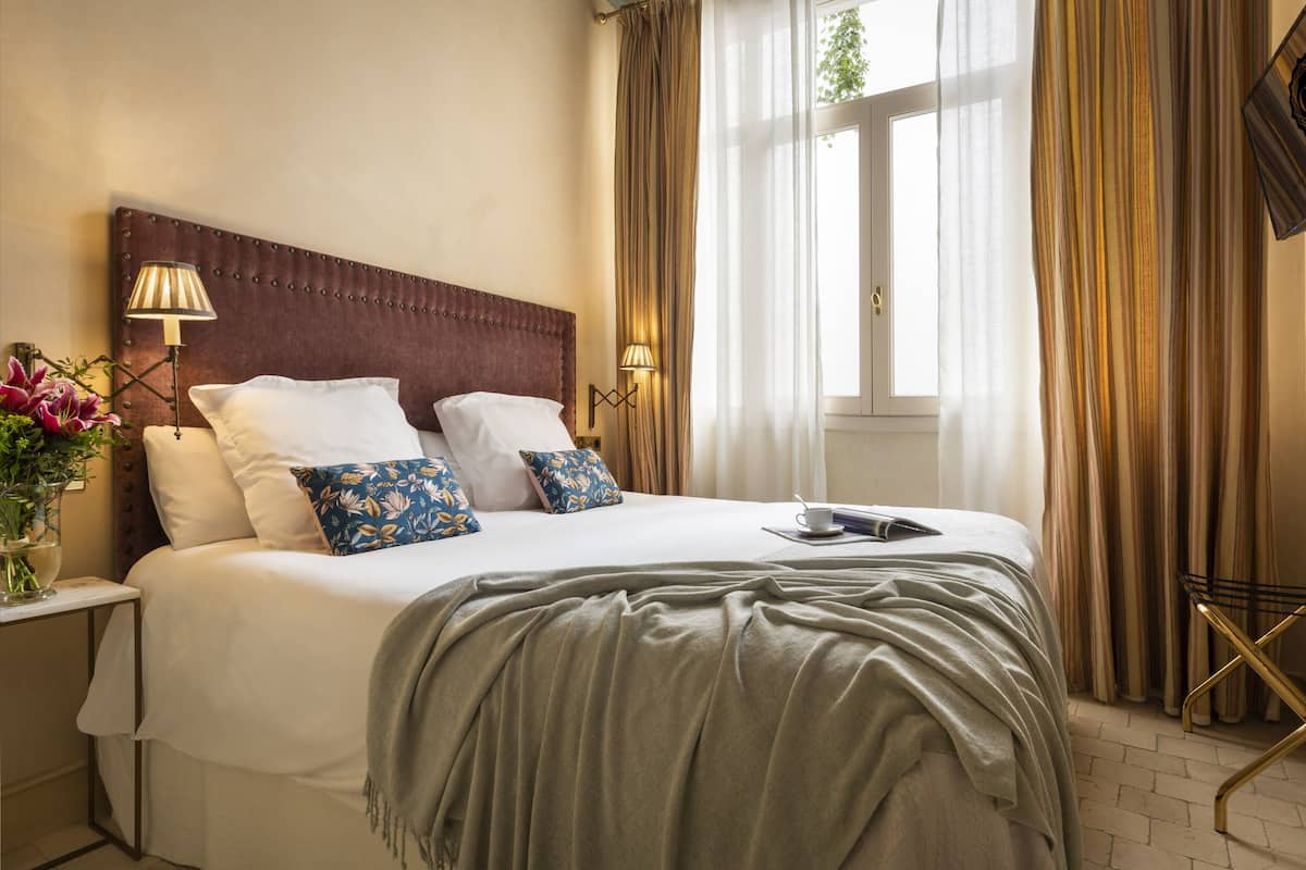 A neatly made bed with a headboard, bedside lamps, and a bedside table with a vase of flowers.