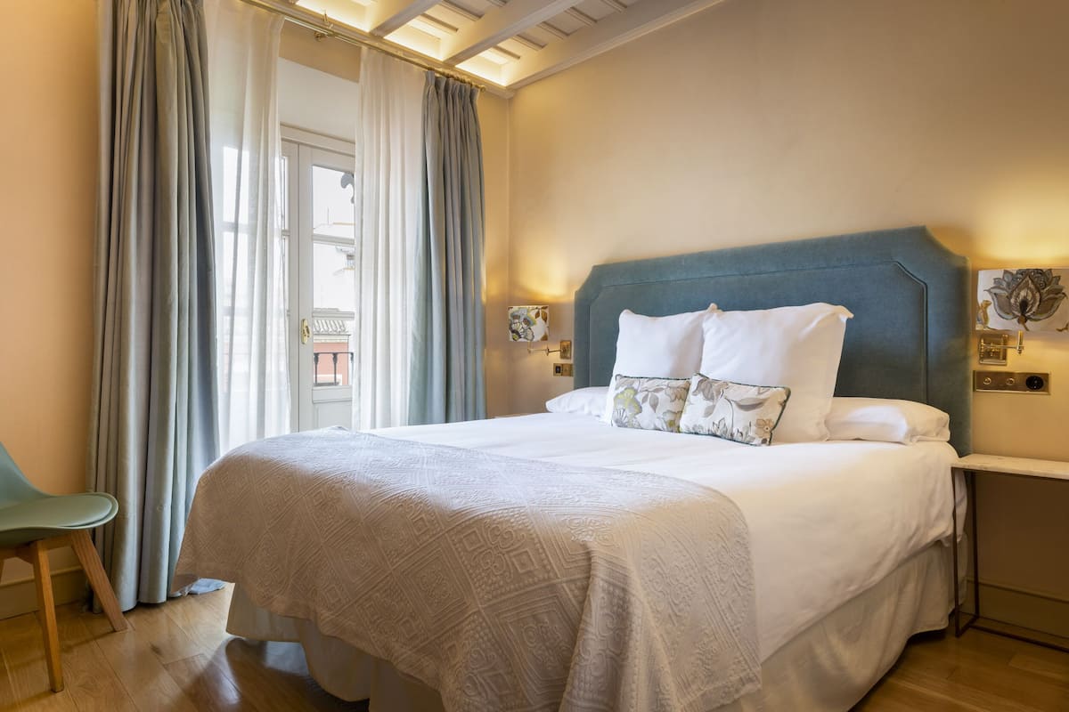 A neatly made bed with a patterned bedspread, a blue upholstered headboard, and two wall-mounted lamps.