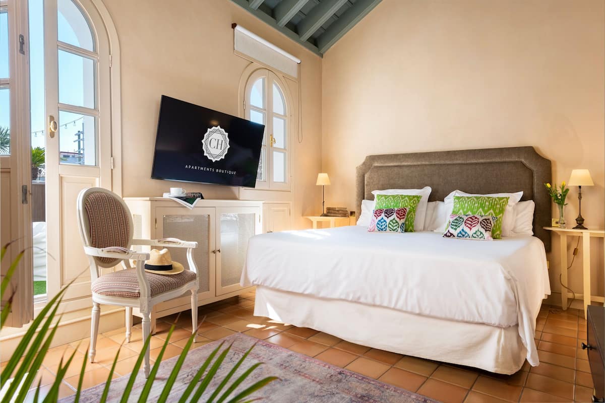 A bedroom with a large bed, a television on the wall, a chair, and a desk.