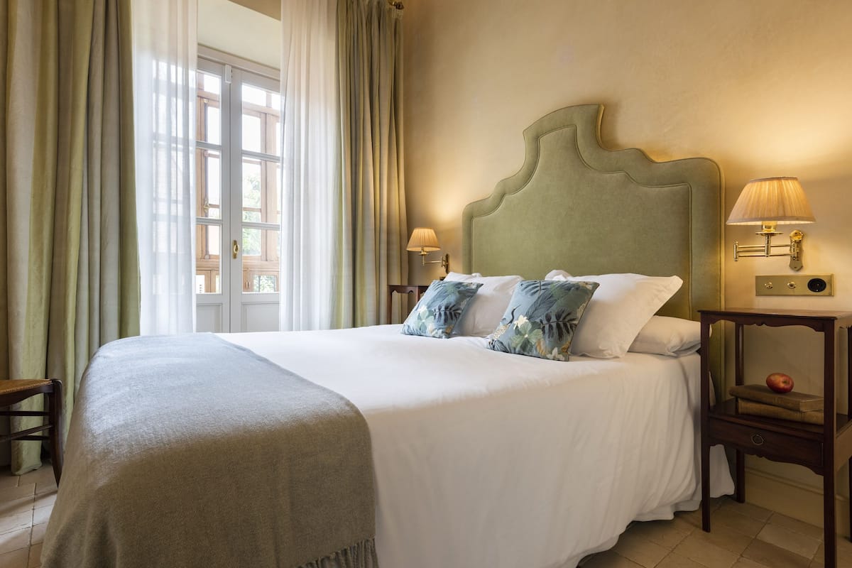 A neatly made bed with a green headboard, two bedside lamps, and a small table with an apple.