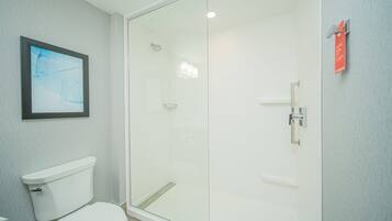 Un baño moderno con cabina de ducha de vidrio, inodoro blanco y un cuadro en la pared.