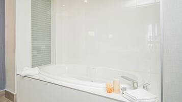 Une salle de bain moderne dotée d’une grande baignoire, d’une douche à parois de verre et d’un meuble-lavabo en verre avec des articles de toilette.