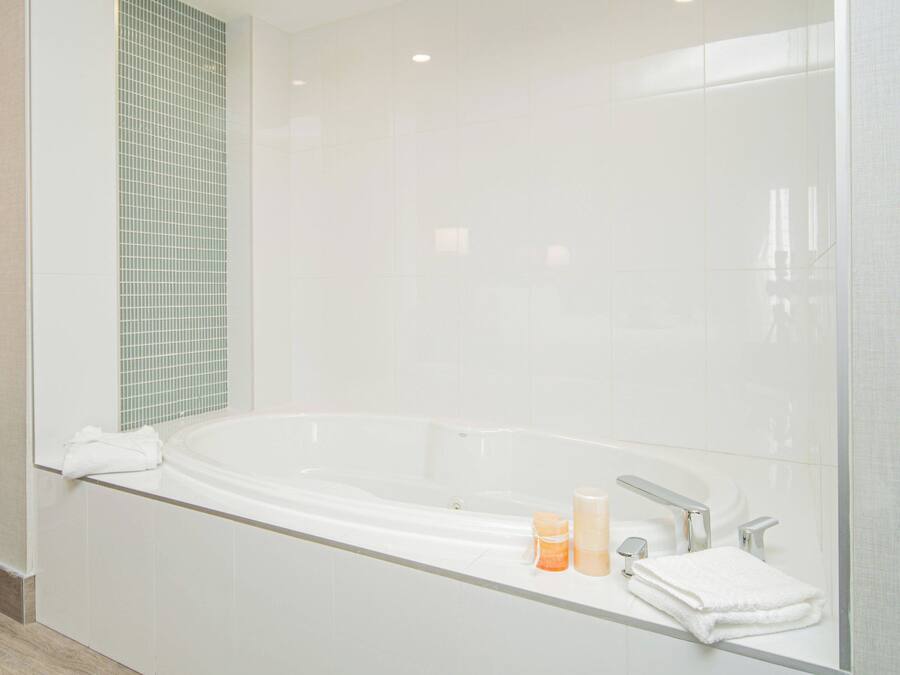 Une salle de bain moderne dotée d’une grande baignoire, d’une douche à parois de verre et d’un meuble-lavabo en verre avec des articles de toilette.