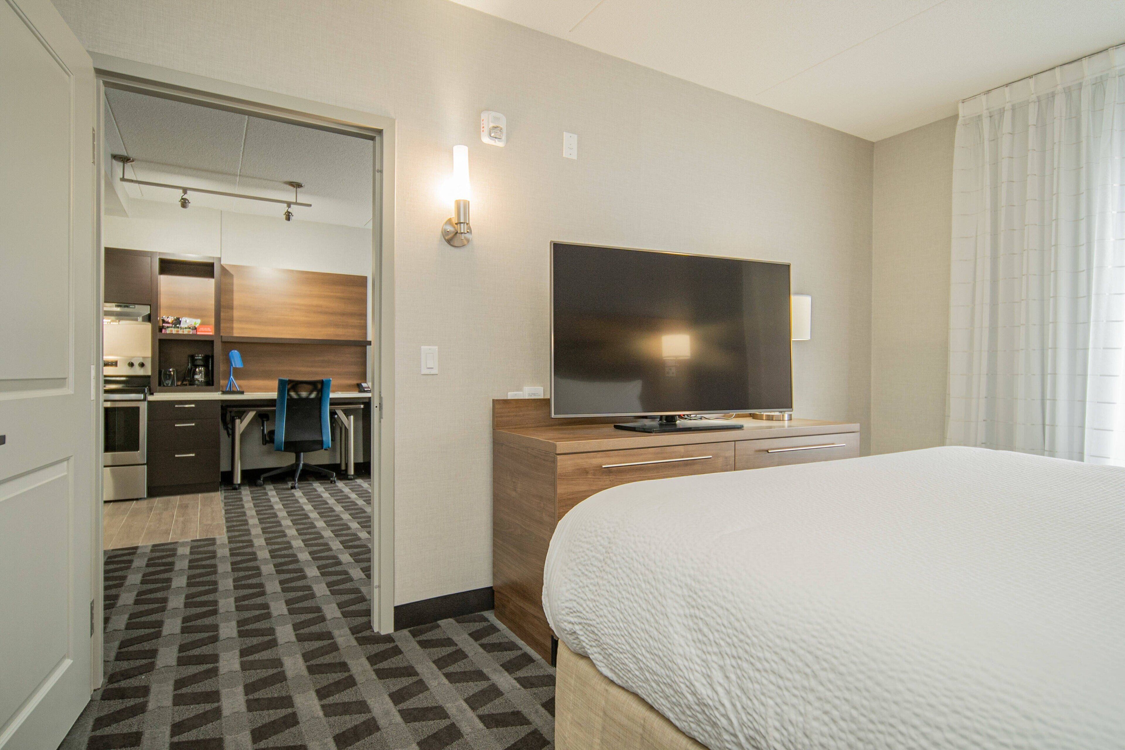 A hotel room with a bed, a TV, a desk with a chair, and a kitchenette.