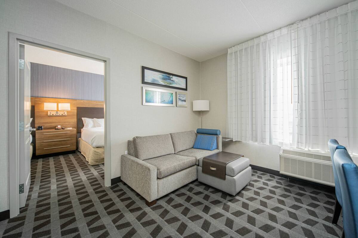 A hotel room with a sofa, a side table, a lamp, and a bed with a headboard.