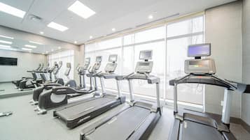 A gym with treadmills, ellipticals, and stationary bikes, large windows, and a modern design.