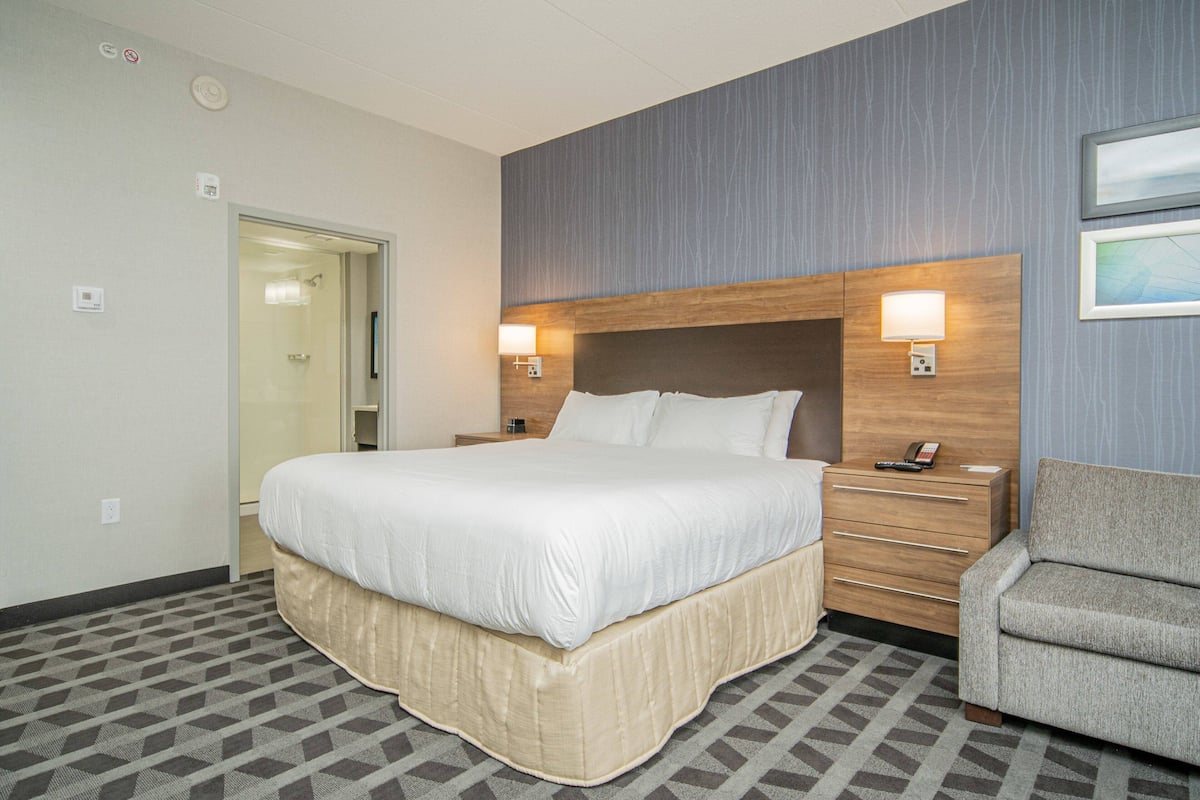 A hotel room with a large bed, bedside lamps, a wooden nightstand, a chair, and a door leading to a bathroom.