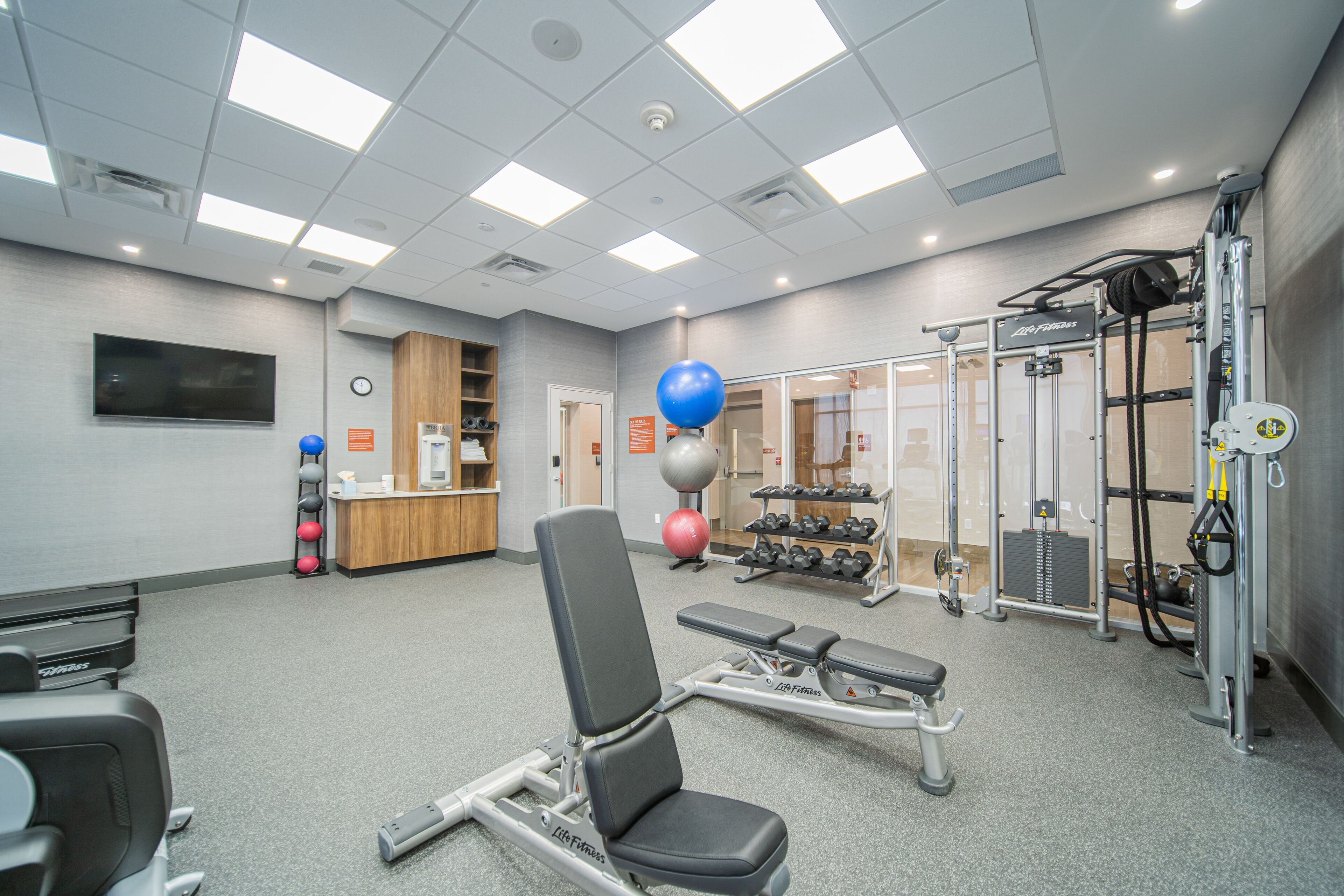 Ein Fitnessraum mit Trainingsgeräten, einer Rezeption und einem an der Wand befestigten Fernseher.