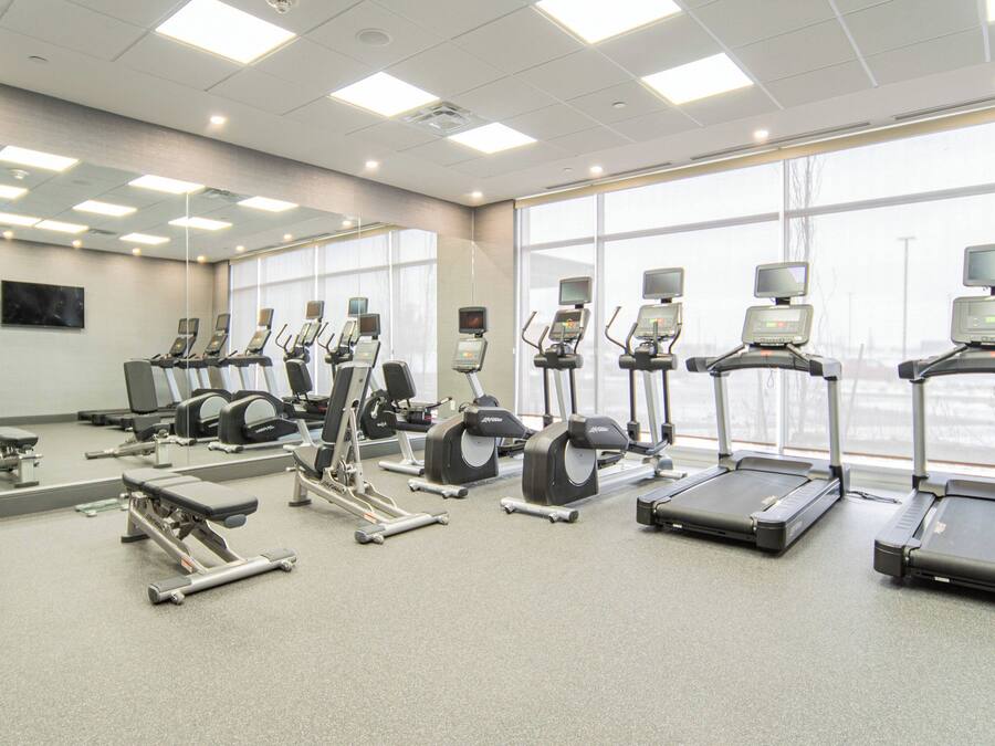A gym with various exercise equipment, large windows, and a mirror on the wall.