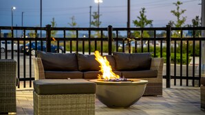An outdoor seating area with a fire feature, wicker furniture, and a metal fence. - TownePlace Suites by Marriott Brantford and Conference Centre (Brantford)