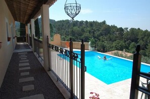 A balcony with a pool, a stone pathway, and a view of a forested area. - Independent apartment in house with pool (Callas)