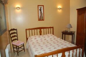A bedroom with a wooden bed, a chair, a bedside table with a lamp, and a wall-mounted picture. - Independent apartment in house with pool (Callas)