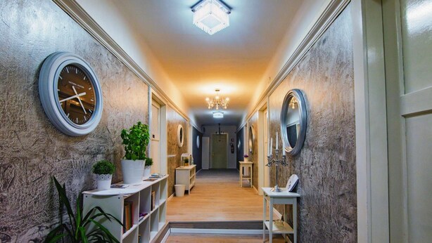 A hallway with a clock, potted plants, and a chandelier. - Mama's and Papa's Luxury Rooms (Split)