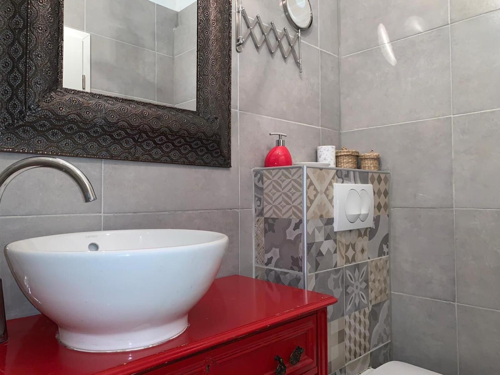 A bathroom with a white sink, red vanity, patterned tiles, a mirror, and a towel dispenser.
