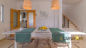 Un coin repas avec une table blanche, des chaises transparentes et un saladier rempli de citrons posé sur la table. Des suspensions en osier sont accrochées au-dessus de la table.