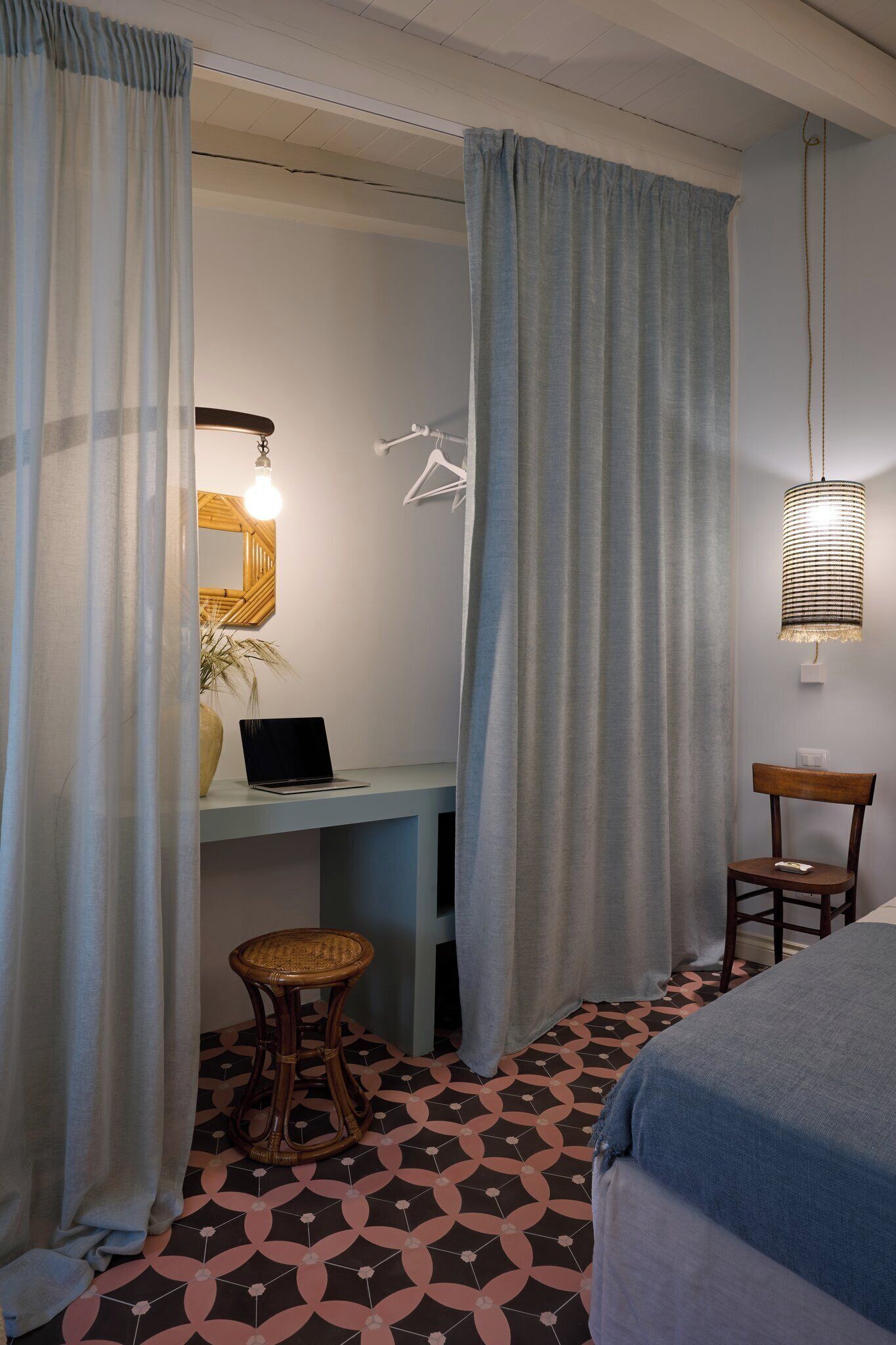 Una habitación con una cama, un escritorio con una computadora portátil, una silla y una lámpara colgante.