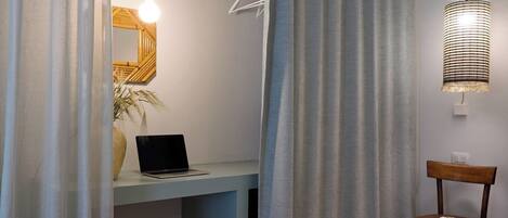 Una habitación con una cama, un escritorio con una computadora portátil, una silla y una lámpara colgante.