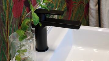 A bathroom sink with a clear glass containing a mint plant, a black faucet, and a white sink.