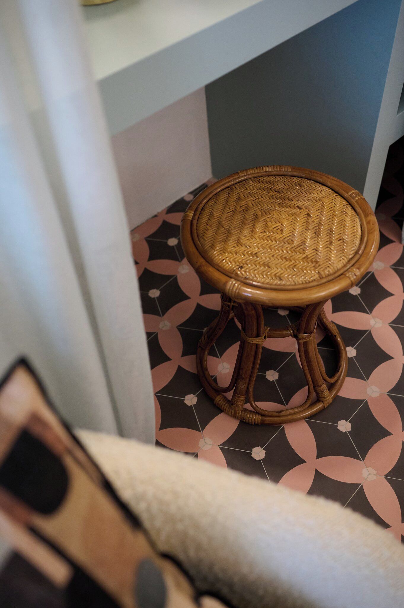 A wicker stool with a woven seat and wooden legs, placed on a patterned floor.