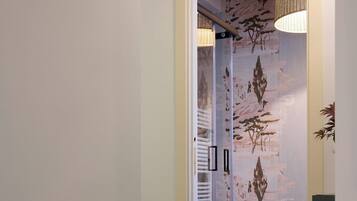 A hallway leading to a bathroom with a glass shower enclosure, a white sink, and a large woven light fixture.