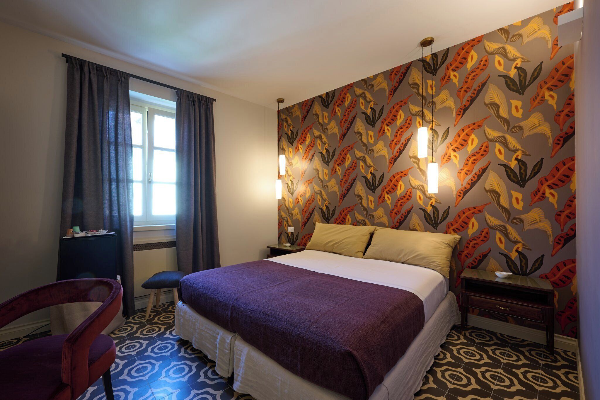 A hotel room with a bed, a chair, a nightstand, a lamp, and a window with curtains.