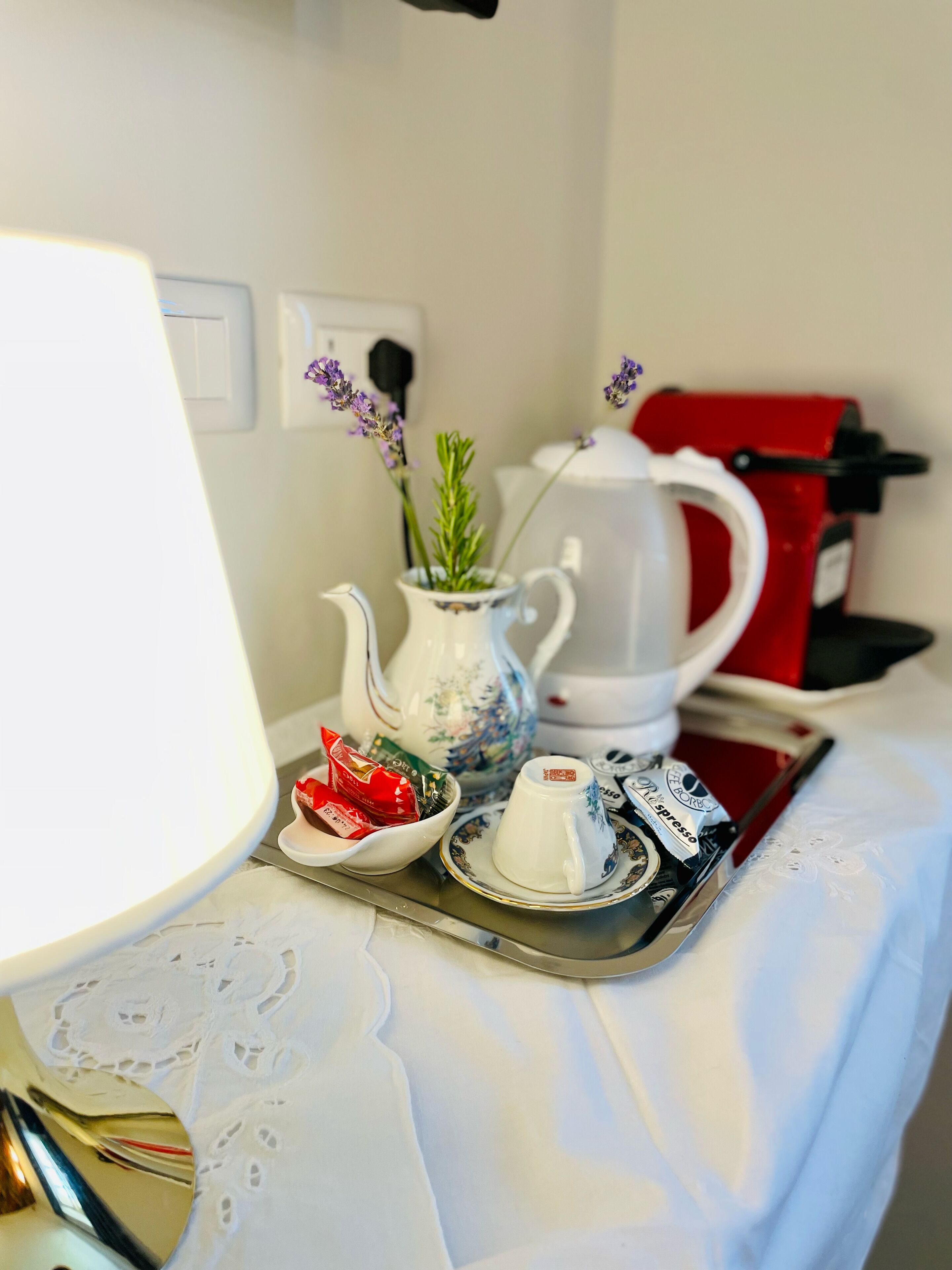 A table with a teapot, a cup, a tray with snacks, and a red coffee machine.