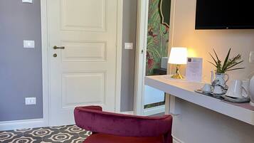Una habitación con puerta blanca, una silla roja, un televisor de pantalla plana, una mesita con lámpara y baldosas de suelo estampadas.