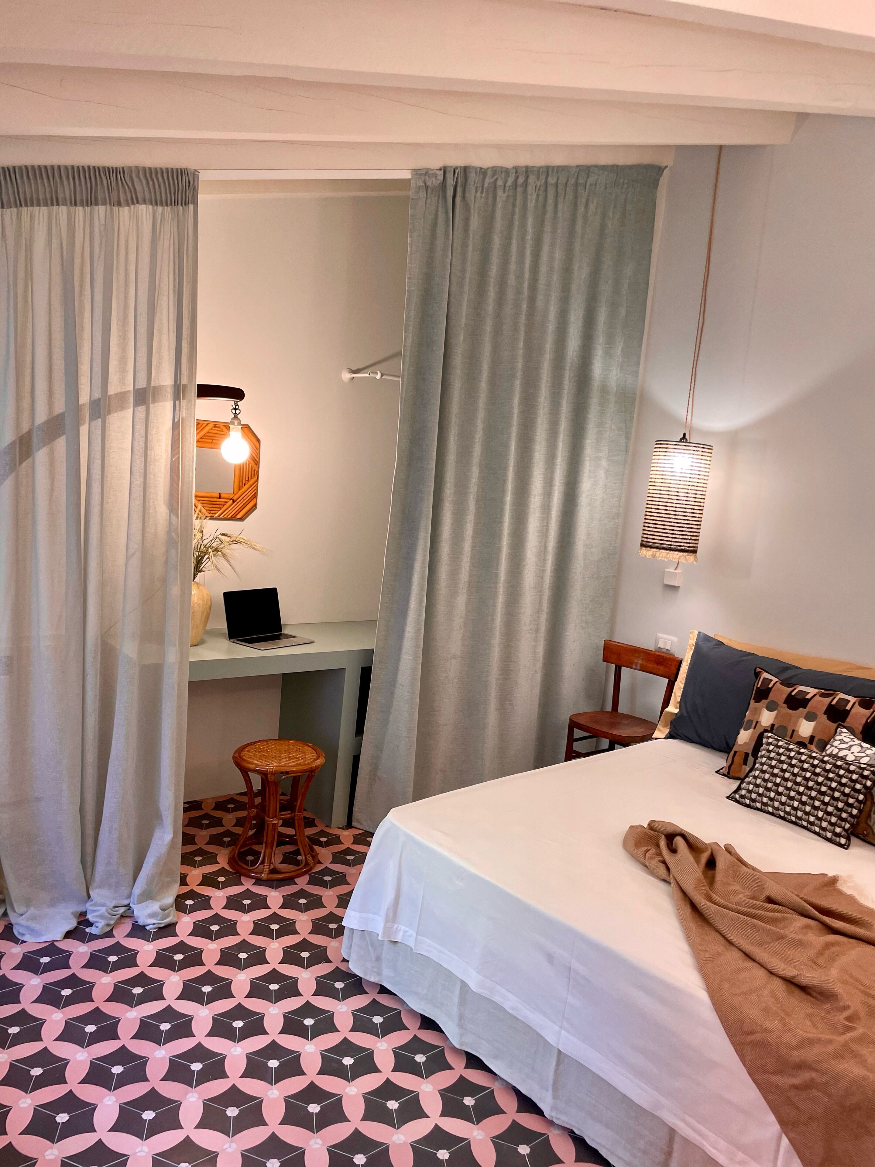 Une chambre d’hôtel avec un lit, un bureau, un ordinateur portable, une chaise et un luminaire suspendu.