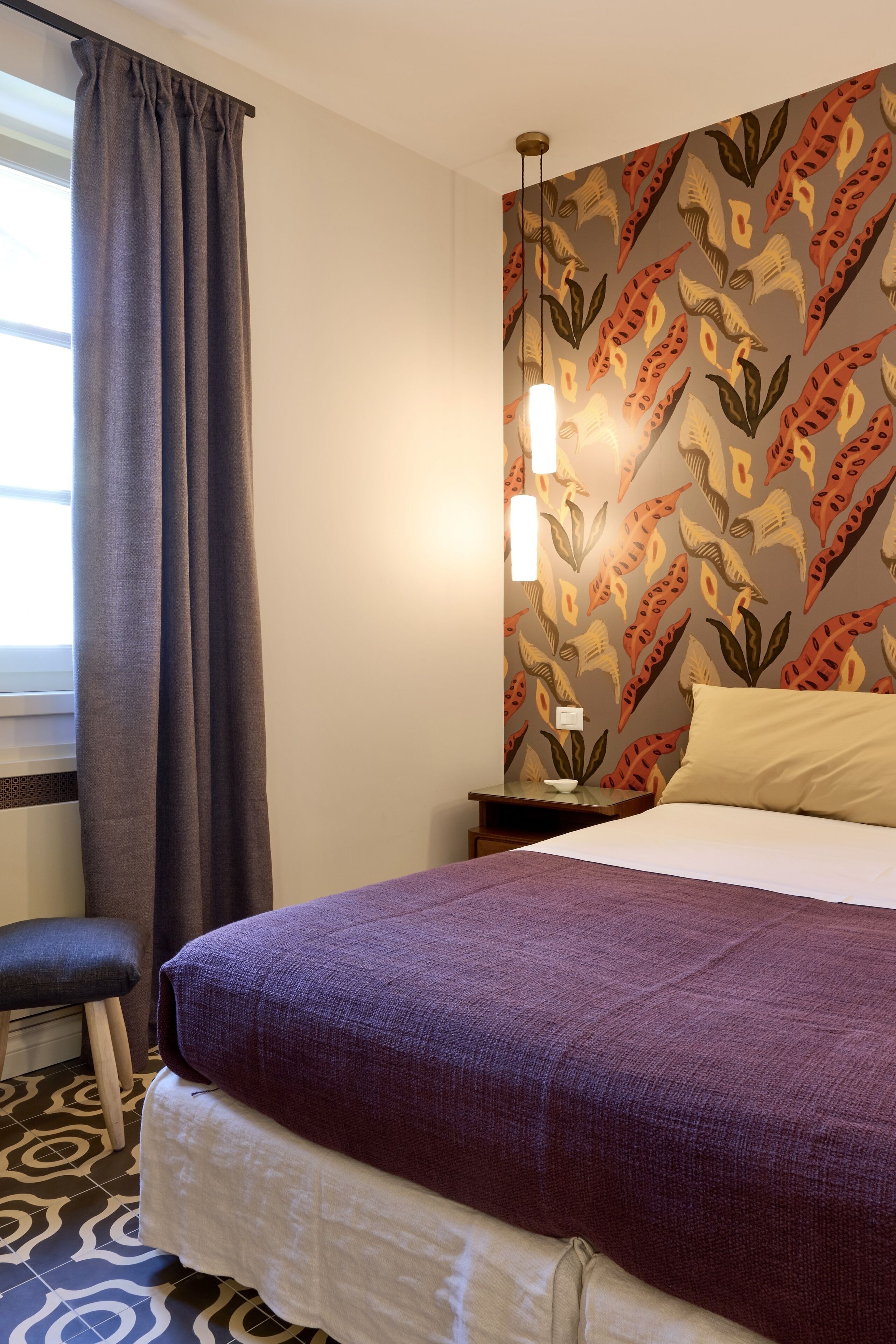 A hotel room with a bed, a nightstand, a chair, and a patterned wall.