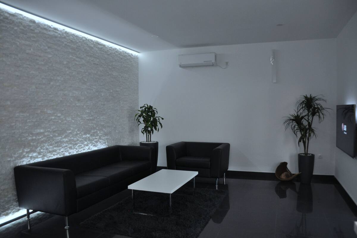 A modern living room with a black sofa, a white coffee table, and two potted plants.