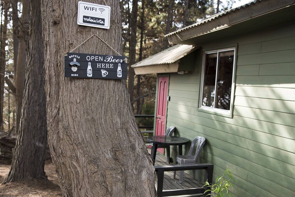 A rustic cabin with a sign indicating WIFI and a password, a sign for open beer, and a small outdoor seating area.